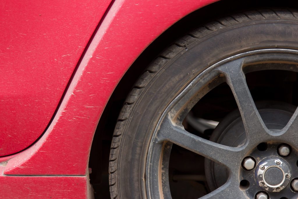 Imagem onde se vê um parte de um pneu de um carro vermelho