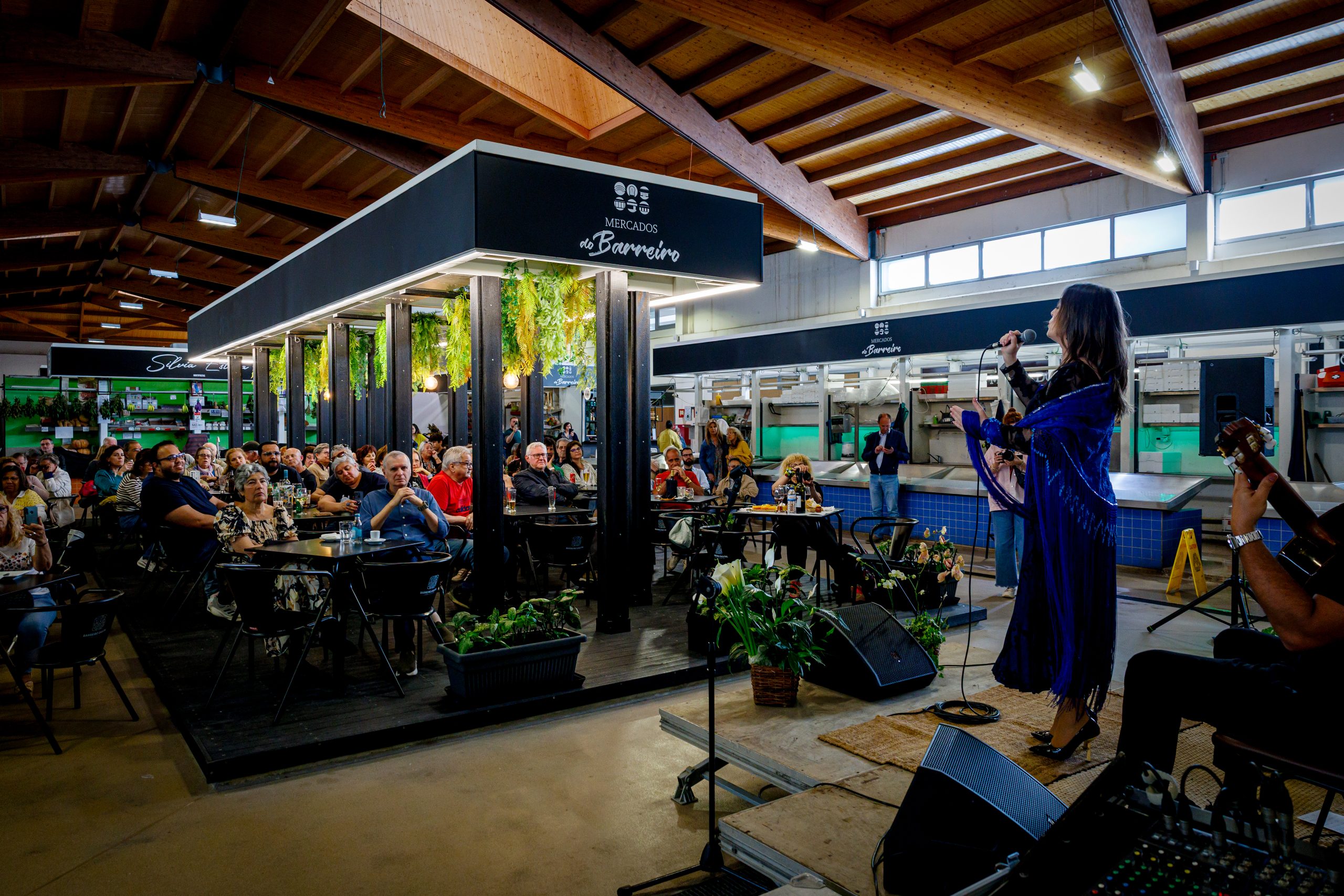 Fotografia de interior do Mercado 1º de Maio com atuação de músicos e pessoas a comer